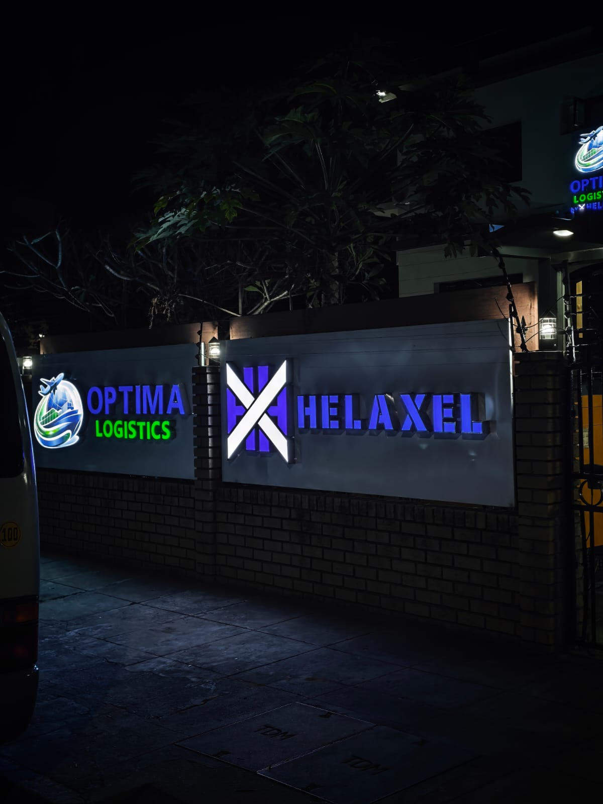 Fachada das instalações da Optima Logistics e Helaxel, com os letreiros iluminados à noite